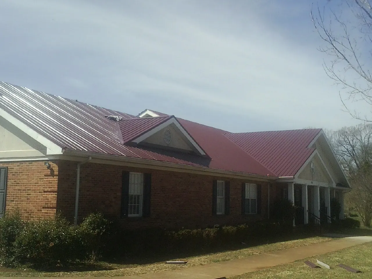 Red metal roof with gabled entries on a long brick building, from a Hail Damage Roof Repair job in Central Point