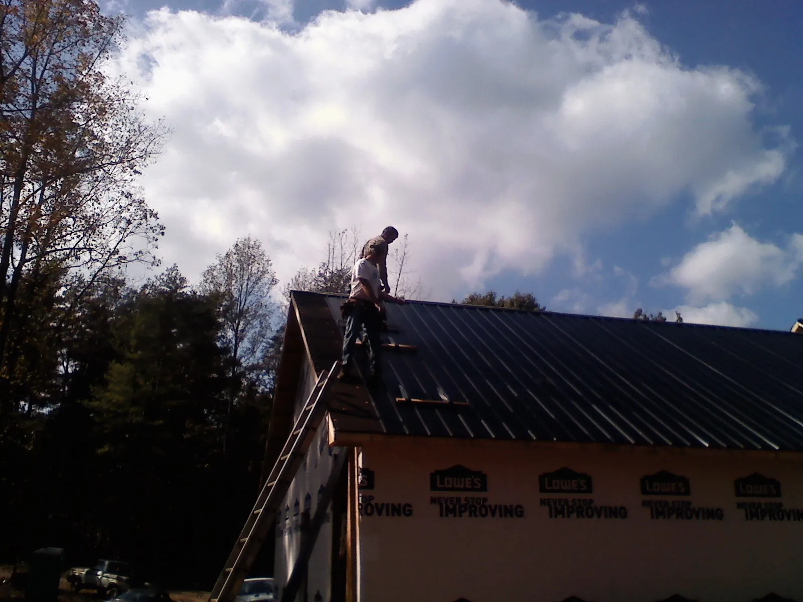 Roofer fastening dark metal panels high against a cloudy sky, from a Roof Inspection job in Central Point